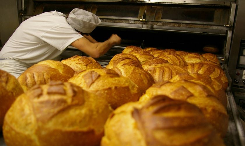 A baker drawing loaves out of the deck oven